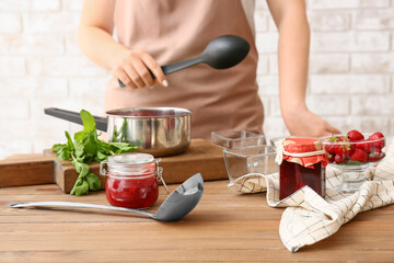 Woman making sweet strawberry jam in kitchen