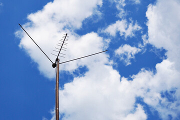 Obraz premium External television antenna on a background of bright blue sky and cotton clouds. Shot in the summer in the country. Vivid illustration about media, TV news and digital broadcasting