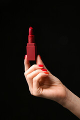 Hand with beautiful manicure holding lipstick on dark background