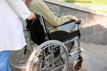 Obraz premium Doctor and young man in wheelchair near stairs outdoors