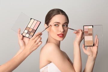 Makeup artist working with beautiful young woman on light background