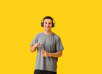 Sporty young man with bottle of water and headphones on color background