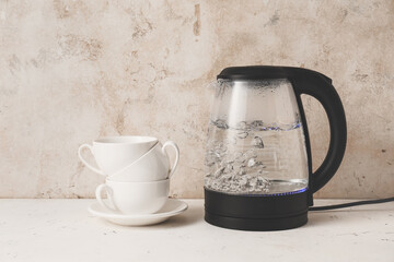 Modern electric kettle and cups on table