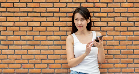 Smiling young woman using a smartphone against brick wall	
