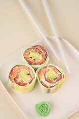 Fresh sushi roll with cucumber, salmon and avocado with chopsticks on a beige background. Healthy food Japanese cuisine. Modern style, top view
