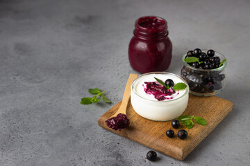 Jar of delicious homemade black currant curd, custard or jam with natural yogurt and fresh berries on grey background. Healthy breakfast.