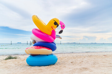 Fancy rubber swim rings on sand beach with blue sea and blue sky background in summer holiday day.