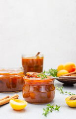 Homemade organic jam in glass jars, ripe apricots, cinnamon and thyme on grey concrete background.