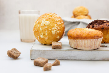 Vanilla muffins and muffins with streusel in paper cups with a glass of milk on light background. Breakfast or snack for children.