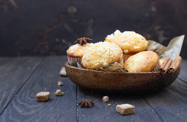 Wooden bowl with tasty homemade muffins, cinnamon, anise star and brown sugar on wooden background. Autumn bakery.