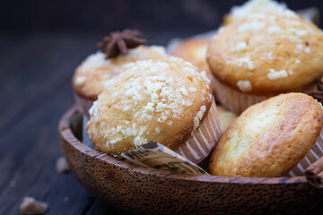 Wooden bowl with tasty homemade muffins, cinnamon, anise star and brown sugar on wooden background. Autumn bakery.