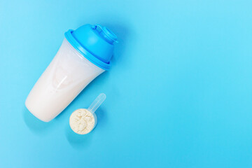 Protein shake and measuring spoon with powdered protein on blue background, a copy of the space