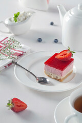 Breakfast. Fresh cheesecake on a white plate with strawberries and mint leaves on a white table. Fresh cottage cheese in a tea set.