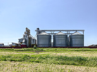 grain elevator, granary. large steel towers for storing crops against clear blue sky background