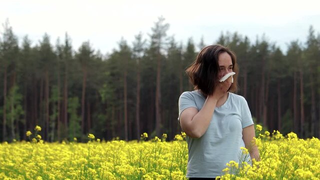 Portrait of a woman with an Allergy in a yellow rapeseed field sneezes into a handkerchief, concept of pollinosis, allergic disease