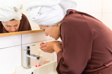 A woman looks in the bathroom mirror. She takes care of her face.