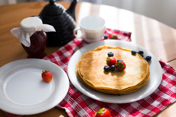 Homemade pancakes with sour cream and fresh berries on white plate on wooden table