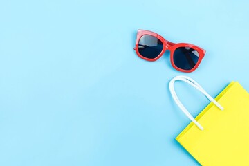 yellow paper shopping bag and red sunglasses on blue background with copy space