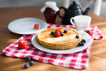 Homemade pancakes with sour cream and fresh berries on white plate on wooden table