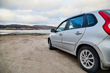 Small car standing on the side of road near wate of lake, river, fiord, sea and ocean.