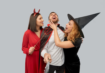 friendship, holiday and people concept - group of happy smiling friends in halloween costumes of witch, devil and vampire having fun taking picture by selfie stick over grey background