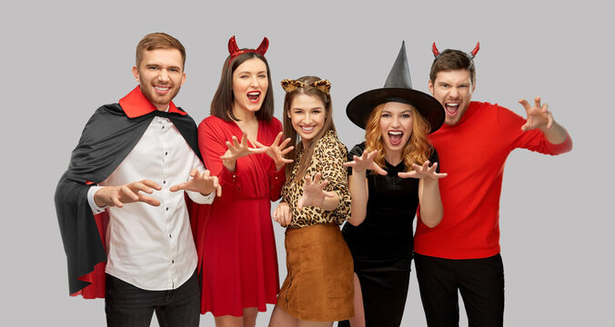 friendship, holiday and people concept - group of happy smiling friends in halloween costumes of vampire, devil, witch and leopard scaring over grey background