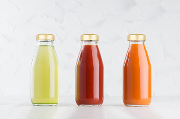 Tomato, carrot, green vegetable juices set in glass bottles with cap mock up in row on white wood table in light interior, template for packaging, advertising, design product, branding.