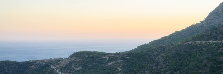 dusk mountain landscape with views of the Mediterranean sea and cloudless sky. Golden hour, haze or fog. banner