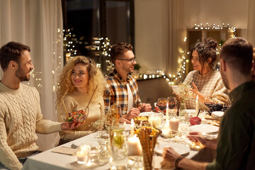 holidays, celebration and people concept - happy smiling friends having christmas dinner party at home in evening
