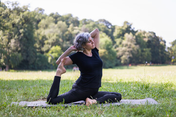 Middle aged woman doing yoga exercises outdoors in the nature. Yoga instructor practicing yoga...