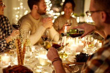 holidays and celebration concept - man pouring red wine into glass at christmas party