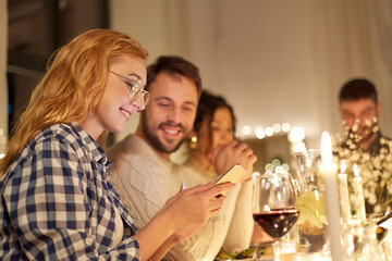 holidays and celebration concept - happy friends with smartphone having christmas dinner party at home