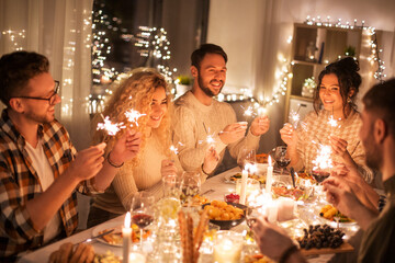 holidays, celebration and people concept - happy friends with sparklers having christmas dinner at home