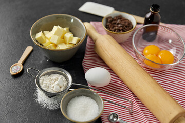 cooking food and culinary concept - rolling pin, butter, eggs, flour and chocolate on table
