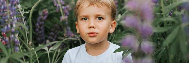 portrait of a cute little happy four year old kid boy with bloom flowers lupines in a field in nature outdoor. banner