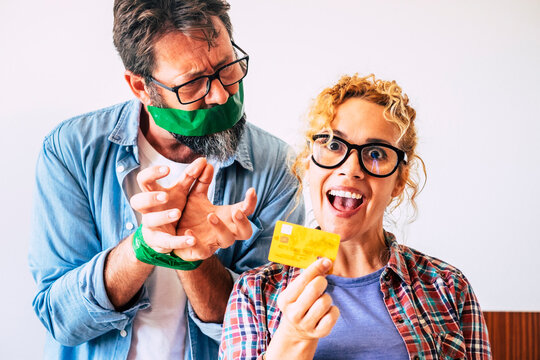 Crazy and cheerful nice beautiful adult woman take bank credit card ready to buy and blocked angry man husband in background - funny economy concept scene at home with people