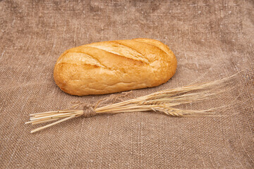Loaf of rye bread or baguette on rustic wooden table with burlap close-up