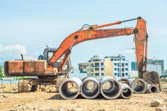 Stack of concrete drainage pipes for wells water discharges laying an external sewage system at a construction site and yellow digger excavator machine equipment. Civil building industry