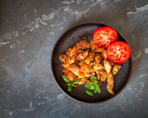 Delicious breakfast with tomatoes and fried chicken meat on a dark plate standing on a gray background
