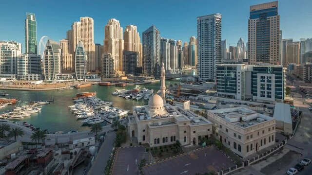 Yachts in Dubai Marina flanked by the Al Rahim Mosque and residential towers and skyscrapers aerial night to day transition timelapse. Modern high rise skyline with boats and wooden dhows