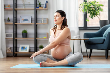 sport and people concept - happy pregnant woman doing yoga at home