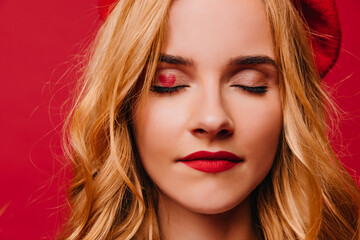 Close-up shot of relaxed beautiful woman in beret. Studio portrait of fair-haired lady with red lips.