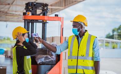 The worker used a medical Digital  temperature Thermometer to check staff body temperature before start work in factory ,they wearing face mask the concept of a corona virus [Covid-19] screening.