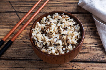 Brown and unpeeled rice on a plate with chopsticks. Wooden rustic background. Copy space.