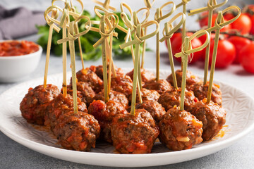 Beef meatballs stewed in tomato sauce on a plate on barbecue skewers. Light concrete background.