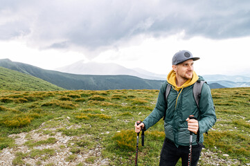 Active backpacker guy engaged nordic walking outdoors. Hipster in cap walks on the footpath on the...