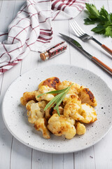 Fried cauliflower florets in batter on a white plate. White wooden background.
