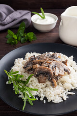 Risotto with mushrooms on a black plate. Boiled white rice with champignons in cream sauce. Dark wooden background. close up