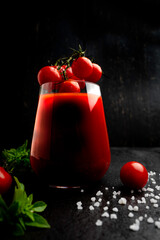 Fresh tomato juice with oregano and a sprig of cherry tomatoes on a dark stone table .