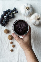 Hand mit Rotwein in einem Glas und herbstliche Kompositon auf einem beigen Leinen Tischtuch. Draufsicht, Nahaufnahme, retro Stil.